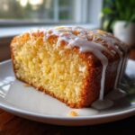 Close-up of a moist slice of Gluten-Free Lemon Coconut Cake topped with white icing and coconut flakes.