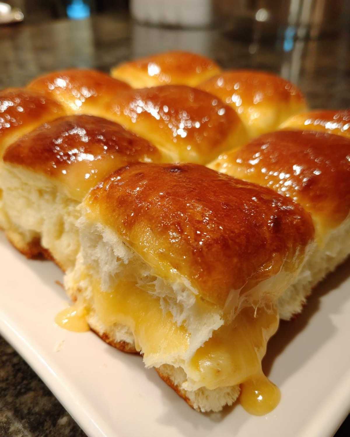 Close-up of Hawaiian Roll Ham and Cheese Sliders showing melted cheese oozing out from the soft rolls glazed with honey mustard.