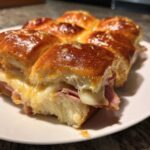 Close-up of baked Hawaiian Roll Ham and Cheese Sliders showing melted cheese oozing out.