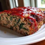 A thick slice of Healthy Turkey Spinach Meatloaf topped with a shiny red glaze, served on a white plate.