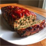 A loaf of Healthy Turkey Spinach Meatloaf, partially sliced, topped with a shiny red glaze.