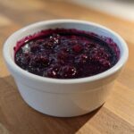 Close-up of thick, deep purple Homemade Blueberry Syrup with whole berries in a small white bowl.
