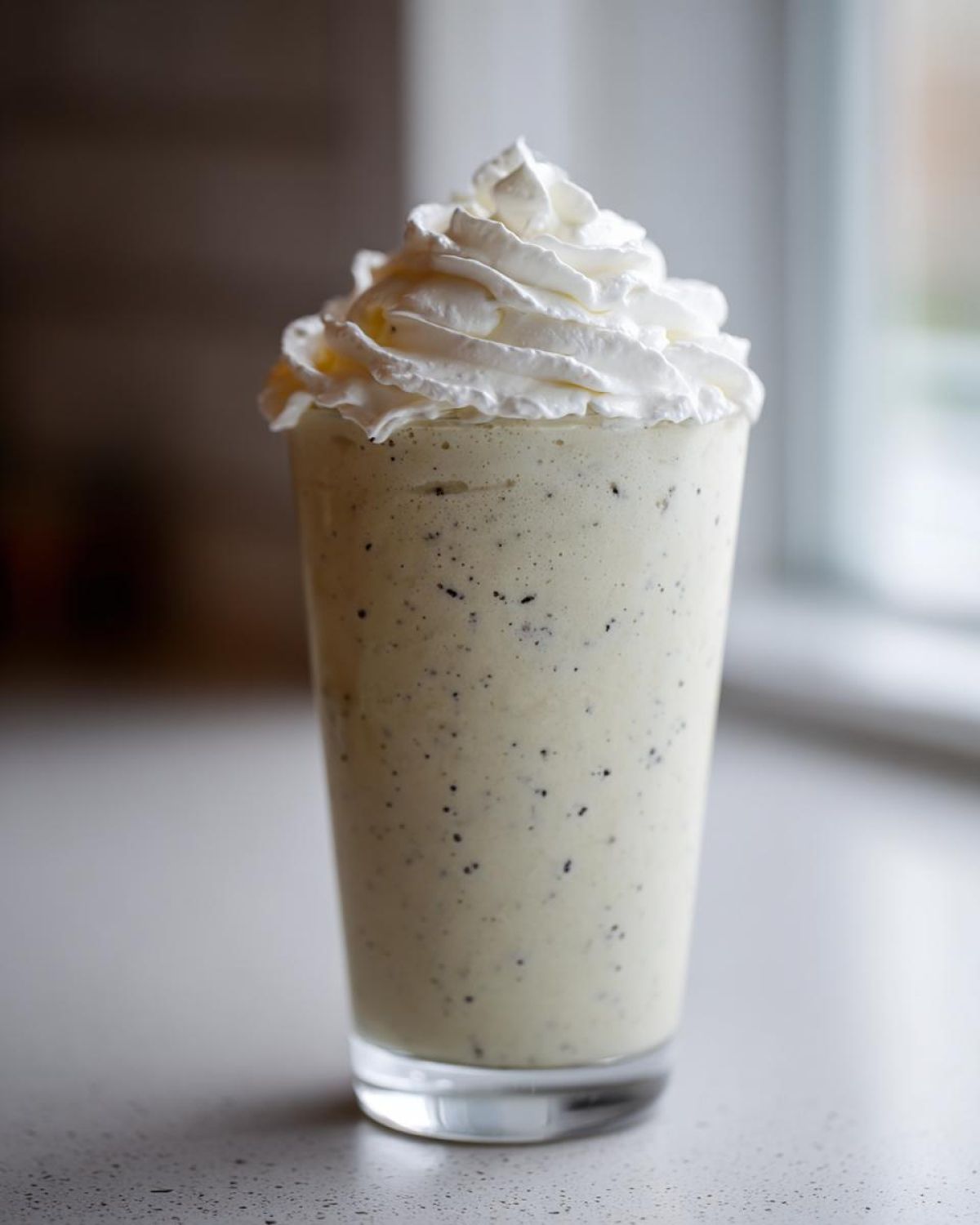 A tall glass of Homemade Vanilla Bean Frappuccino topped with a swirl of whipped cream.