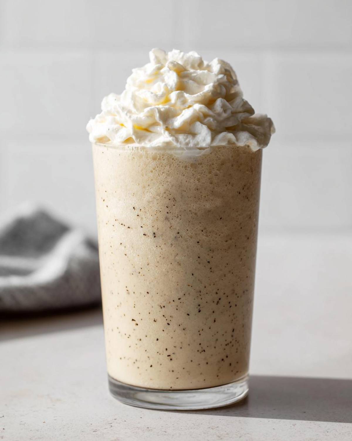 A tall glass of Homemade Vanilla Bean Frappuccino topped high with whipped cream.