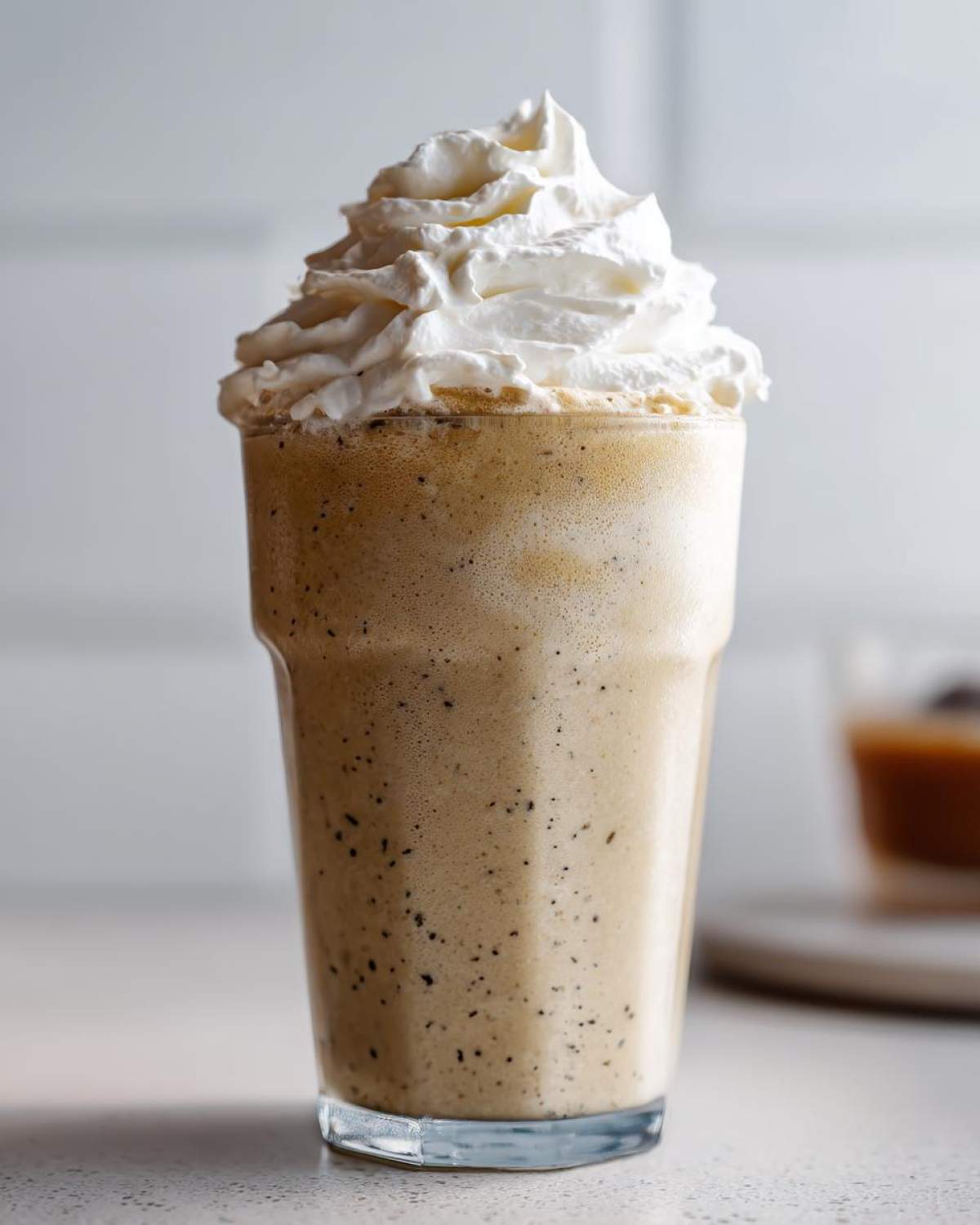A tall glass filled with a blended Homemade Vanilla Bean Frappuccino topped generously with whipped cream.