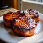 Three thick, round Honey Glazed Ham Steak in the Skillet portions glistening with a dark, caramelized honey glaze on a white plate.