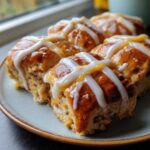 Close-up of freshly baked Hot Cross Buns with Orange Glaze drizzled across the top, sitting on a light blue plate.