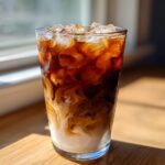 A tall glass of Iced Brown Sugar Oatmilk Latte showing layers of dark espresso swirling into creamy oatmilk over ice.