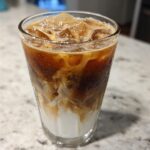 Close-up of a tall glass filled with an Iced Honey Almond Milk Latte, showing layers of almond milk, espresso, and ice.