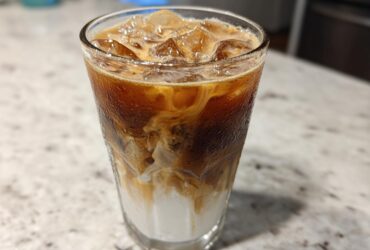 Close-up of a tall glass filled with an Iced Honey Almond Milk Latte, showing layers of almond milk, espresso, and ice.