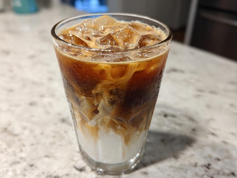 Close-up of a tall glass filled with an Iced Honey Almond Milk Latte, showing layers of almond milk, espresso, and ice.