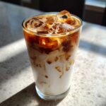 Close-up of a tall glass filled with an Iced Honey Almond Milk Latte, showing rich espresso swirling into white almond milk over ice.