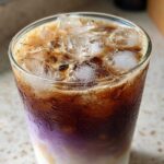 Close-up of a refreshing Iced Lavender Latte showing distinct layers of milk, purple syrup, and dark espresso over ice.