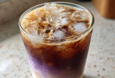 Close-up of a refreshing Iced Lavender Latte showing distinct layers of milk, purple syrup, and dark espresso over ice.