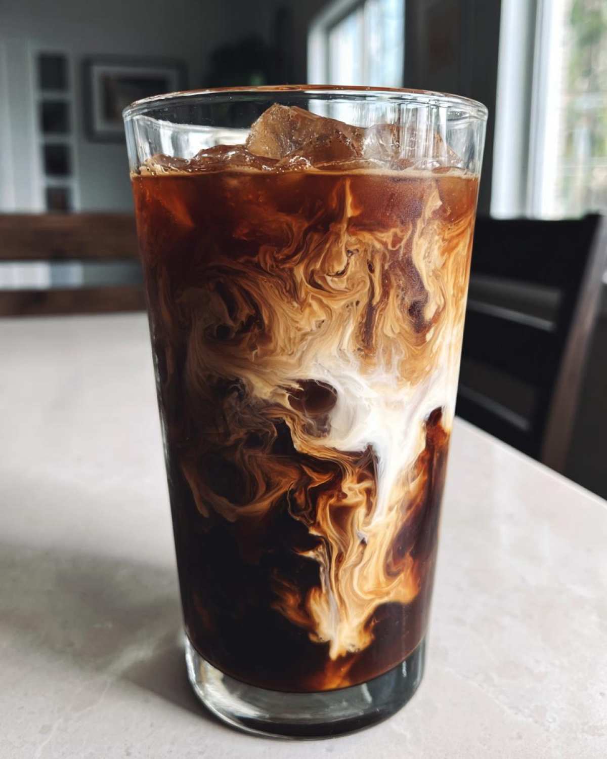 Close-up of a tall glass filled with an Iced Mocha, showing dramatic swirls of cream mixing into the dark coffee.