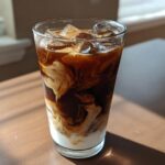 Close-up of an Iced Mocha showing rich dark coffee swirling beautifully with white milk over ice cubes.