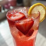 Close-up of a tall, sweating glass filled with Iced Strawberry Lemon Tea, sliced strawberries, and a lemon wheel garnish.