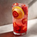 A tall, sweating glass filled with Iced Strawberry Lemon Tea, loaded with fresh strawberries and a lemon slice.