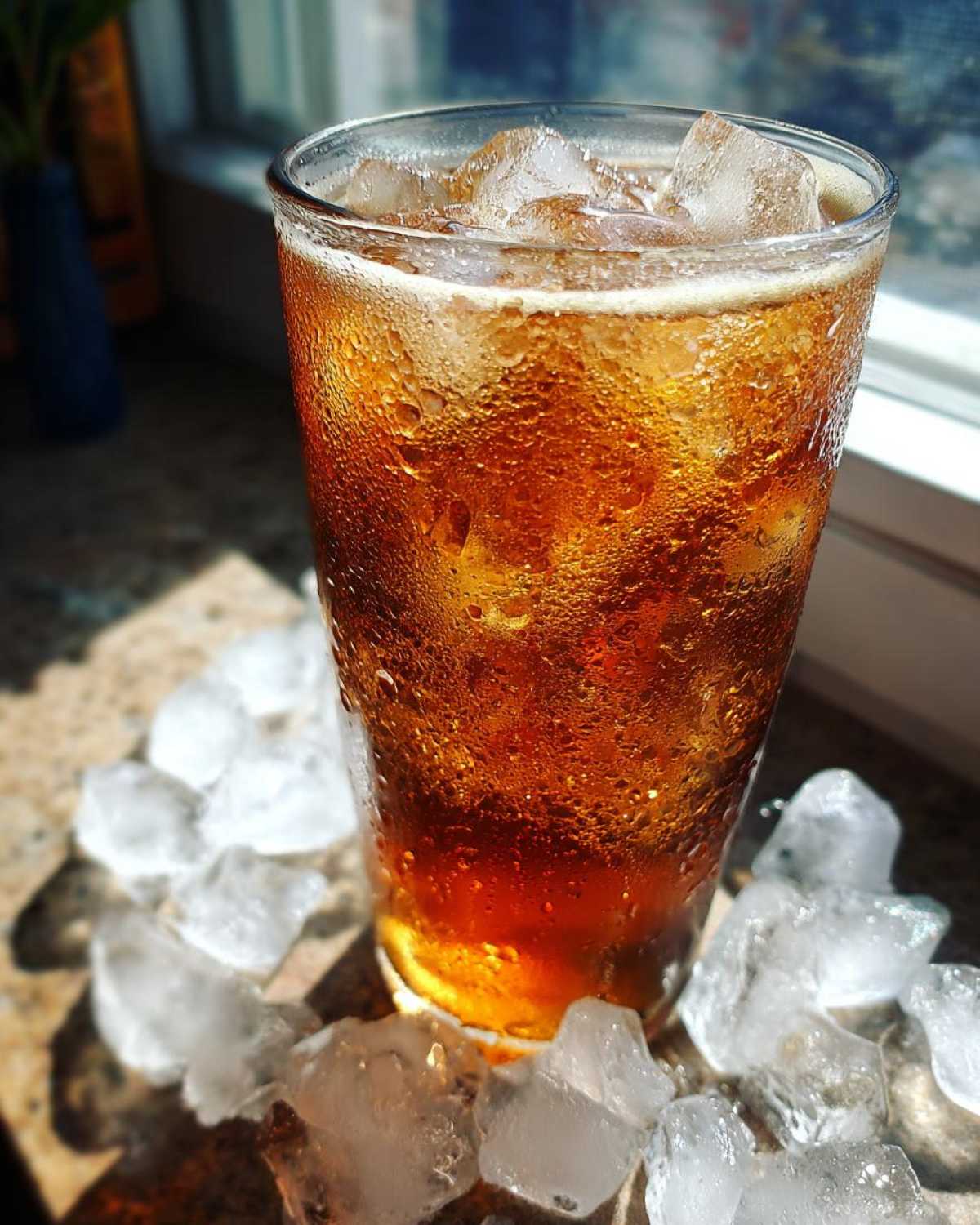 A tall glass filled with a cold Iced Vanilla Chai Latte, covered in condensation and surrounded by ice cubes.
