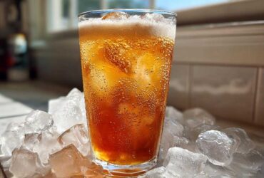 A tall glass filled with a bubbly, amber-colored Iced Vanilla Chai Latte, surrounded by large ice cubes.