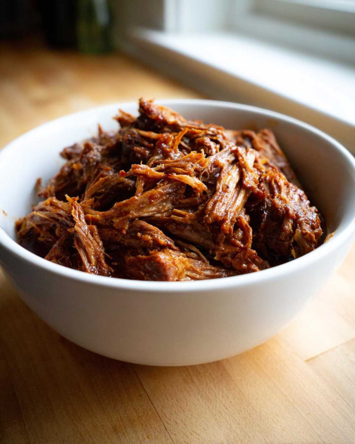 Close-up of tender, shredded Instant Pot Beef Barbacoa coated in rich sauce, served in a white bowl.