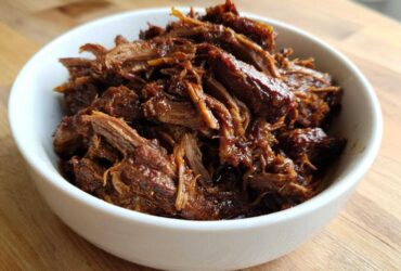 A white bowl filled with richly seasoned, shredded Instant Pot Beef Barbacoa resting on a wooden surface.