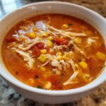 Close-up of a white bowl filled with vibrant orange Instant Pot Chicken Tortilla Soup, showing shredded chicken, corn, and tomatoes.