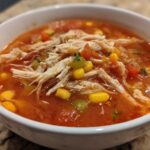 Close-up of a white bowl filled with Instant Pot Chicken Tortilla Soup, featuring shredded chicken, corn, and tomatoes.