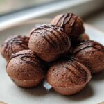A stack of rich, dark brown Keto Chocolate Peanut Butter Fat Bombs drizzled with melted chocolate.