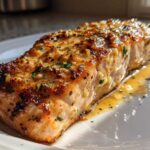 A close-up of a glistening, pan-seared Keto Garlic Butter Salmon fillet resting in its sauce on a white plate.