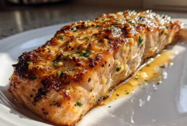 A close-up of a glistening, pan-seared Keto Garlic Butter Salmon fillet resting in its sauce on a white plate.