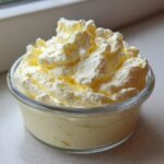 Close-up of a single serving of light yellow Keto Lemon Cheesecake Mousse topped with whipped cream.