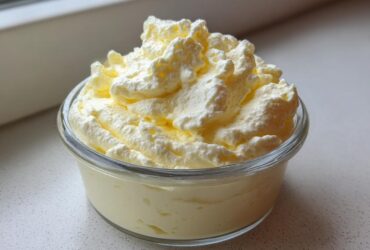 Close-up of a single serving of light yellow Keto Lemon Cheesecake Mousse topped with whipped cream.