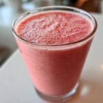 Close-up of a tall glass filled with a thick, pink Keto Strawberry Cheesecake Smoothie, showing a frothy top.
