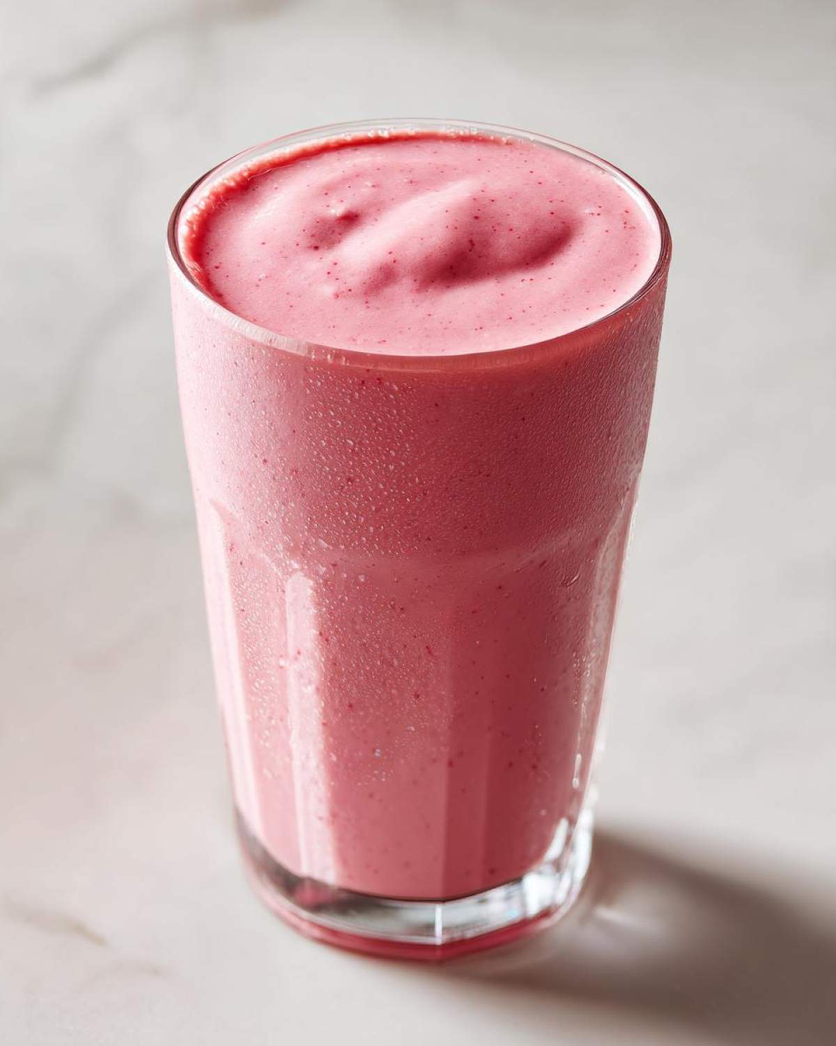 A tall glass filled with a thick, pink Keto Strawberry Cheesecake Smoothie, showing condensation on the glass.