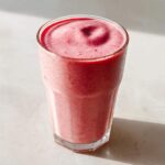 A tall glass filled with a thick, pink Keto Strawberry Cheesecake Smoothie, showing a swirl on top.