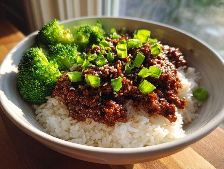 A close-up of Korean Ground Beef Bulgogi Bowls featuring saucy ground beef over white rice, topped with green onions and sesame seeds, served with steamed broccoli.