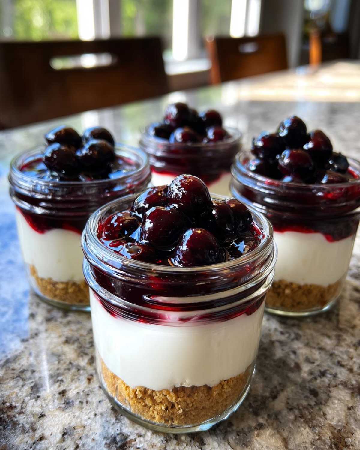 Four individual Lemon Blueberry Cheesecake Jars layered with graham cracker crust, creamy filling, and topped with blueberry compote.