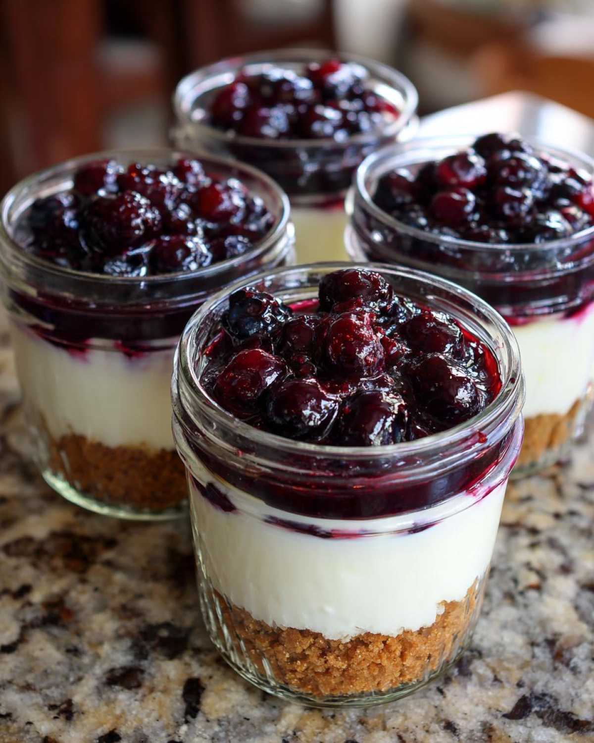 Four individual servings of Lemon Blueberry Cheesecake Jars layered with graham cracker crust, creamy filling, and blueberry topping.