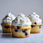 Three Lemon Blueberry Cupcakes with tall swirls of white cream cheese frosting.