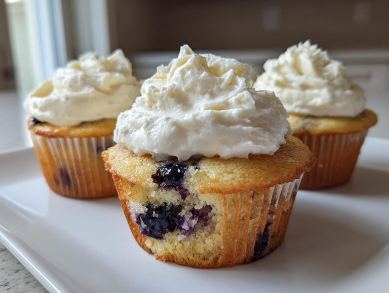 Three Lemon Blueberry Cupcakes with thick swirls of cream cheese frosting on a white plate.