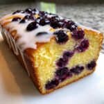 Close-up of a slice of moist Lemon Blueberry Yogurt Loaf topped with a thick lemon glaze and fresh blueberries.