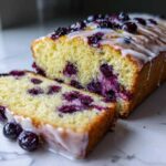 A slice cut from a moist Lemon Blueberry Yogurt Loaf topped with a white glaze and fresh blueberries.