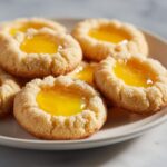 A close-up of several bright, buttery Lemon Curd Thumbprint Cookies filled with glossy yellow lemon curd.