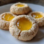 Four delicious Lemon Curd Thumbprint Cookies with bright yellow filling resting on a white plate.