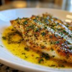 Close-up of a flaky Lemon Garlic Butter Tilapia fillet swimming in rich, herbed butter sauce.