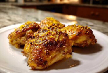 Four perfectly roasted Lemon Garlic Roasted Chicken Thighs topped with bright orange zest on a white plate.
