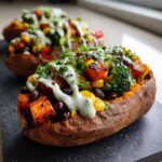 Close-up of a Loaded Veggie Stuffed Sweet Potato topped with black beans, corn, broccoli, and a creamy green sauce.
