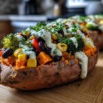 Close-up of a Loaded Veggie Stuffed Sweet Potato topped with corn, black beans, broccoli, and a creamy herb sauce.