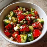 Close-up of a bowl of Mediterranean Cucumber Tomato Salad tossed in dressing with feta cheese.